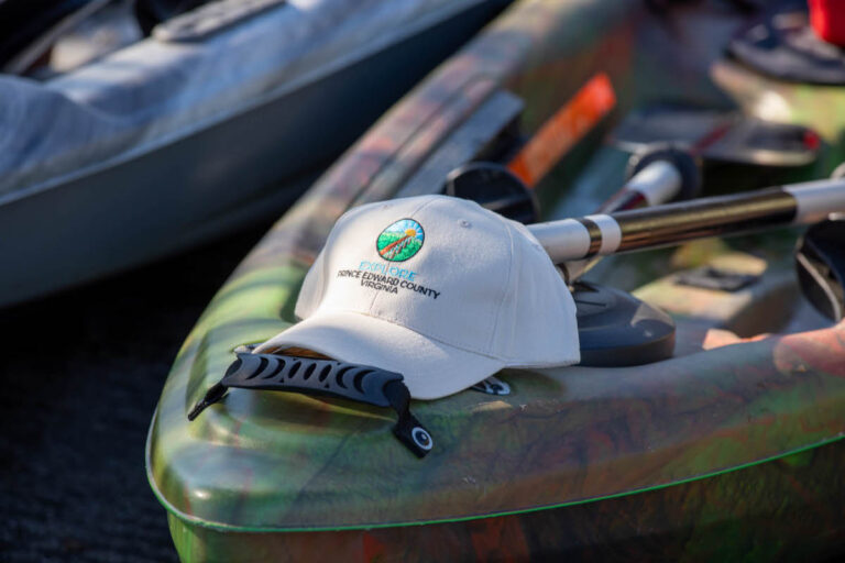 A baseball cap with the phrase "Explore Prince Edward County, Virginia" sitting on the front of a kayak.