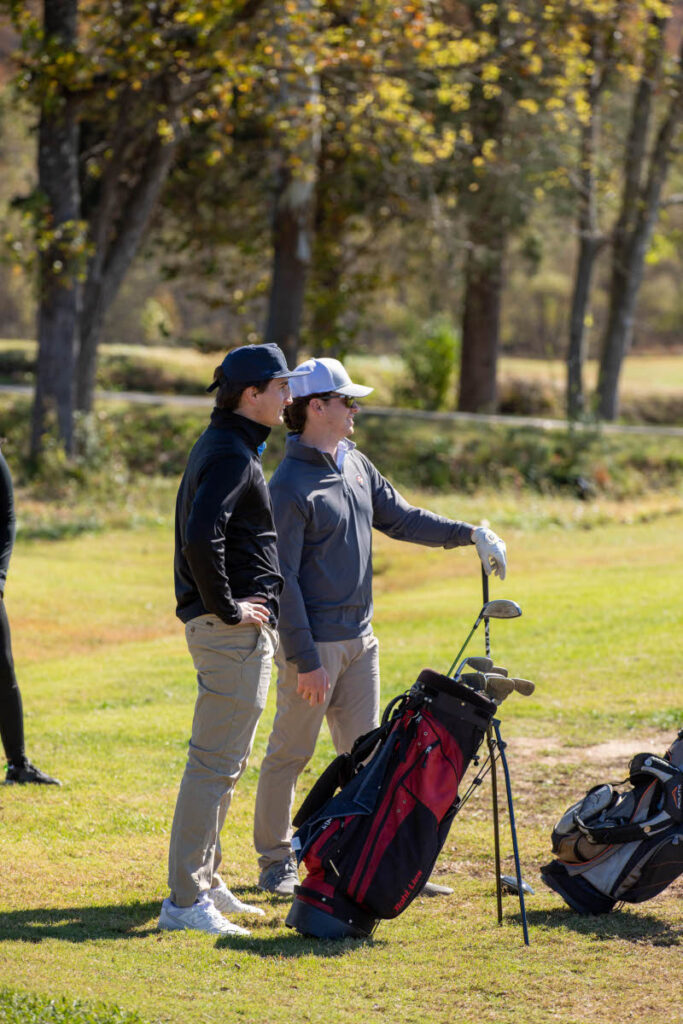 Two men standing on a golf course with their golf bags on a sunny day.